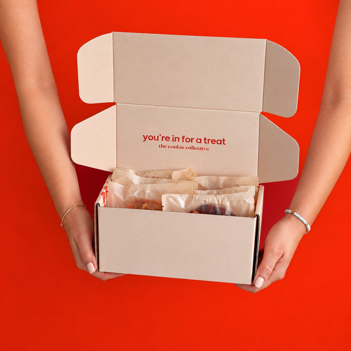 An open Cookie Collective box of individually wrapped cookies, held up against a red background